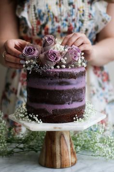 a woman is decorating a chocolate cake with purple frosting and flowers on top