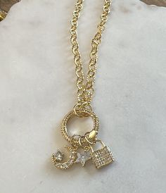 Elevate your outfit with our gold Dreamer Charm Necklace. 18k gold dipped chain with a trio of 24k gold filled charms with clear stone details. Charms include a moon, a star and a lock nestled on a rhinestone pave O ring! You can change out your charms with the clasp O ring charm holder. Comes with charms seen in photo. We ship across the US! Trendy Gold Charm Necklace With Moon Charm, Gold Cubic Zirconia Necklace With Star Charm, Gold Necklace With Moon Charm And Cubic Zirconia, Gold Necklace With Moon Charm In Cubic Zirconia, Gold-plated Charm Necklace With Star Charm, Gold Plated Charm Necklace With Star Charm, Everyday Gold-plated Charm Necklace With Star Charm, Everyday Gold Plated Charm Necklace With Star Charm, Gold-plated Star Charm Necklace