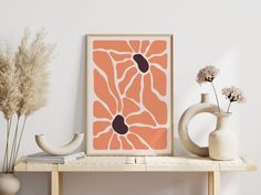 an orange and black art print on a shelf next to vases with dried flowers