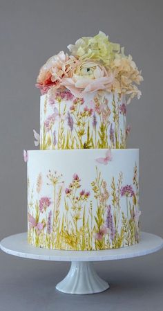 a three tiered cake decorated with flowers and butterflies on a white pedestal, against a gray background