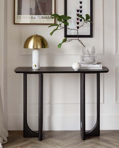 a black and gold console table with a plant on it in front of a white wall