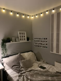 an unmade bed in a bedroom with string lights on the wall and pictures above it