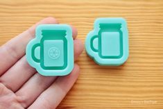 two green plastic cups sitting next to each other on a wooden table in front of a person's hand