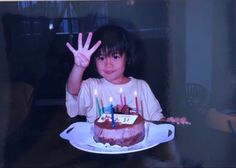 a young boy holding up a birthday cake with lit candles on it in front of him