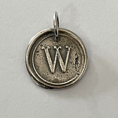 a silver wax seal with the letter w on it's side, hanging from a chain