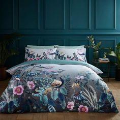 a bed with blue walls and flowers on the comforter, next to a potted plant