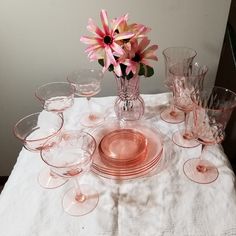 a table topped with lots of pink glassware and a vase filled with flowers on top of a white cloth