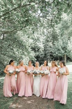 a group of women standing next to each other in front of trees and grass with bouquets