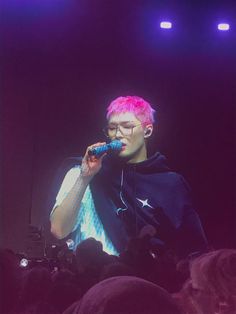 a man with pink hair and glasses on singing into a microphone in front of an audience