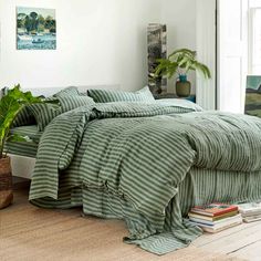 a bed with green and white striped comforter next to a potted plant on the floor