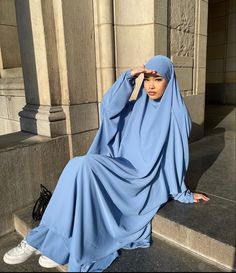 a woman in a blue hijab sitting on steps with her hands behind her head