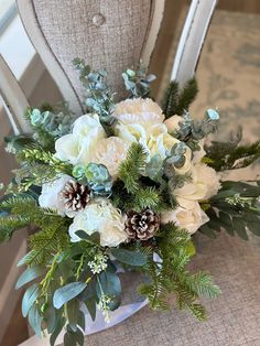 a bouquet of flowers sitting on top of a chair with pine cones and greenery