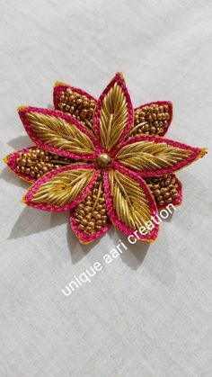 a gold and pink flower brooch sitting on top of a white cloth