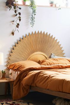 a bed with an orange bedspread in a bedroom next to a window and potted plants