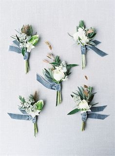 six boutonnieres with white flowers and greenery are arranged on a gray surface