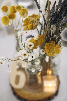 a vase filled with yellow and white flowers on top of a wooden table next to a candle