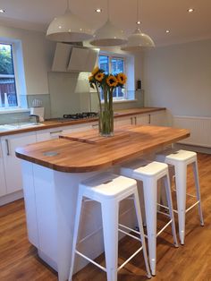 a kitchen island with three stools in front of it and sunflowers on the counter