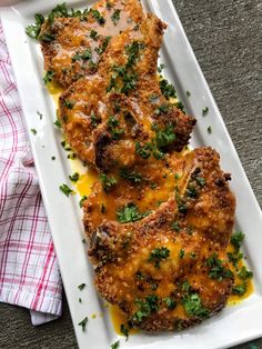 two pieces of meat covered in cheese and parsley on a white platter next to a napkin