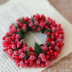 a wreath made out of red berries and green leaves on top of an open book