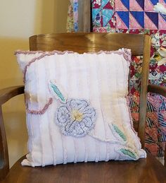 a pillow sitting on top of a wooden chair next to a quilted wall hanging