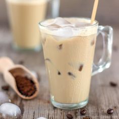 two glasses filled with iced coffee on top of a wooden table next to spoons