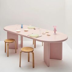 a pink table with two stools and plates on it in front of a white wall