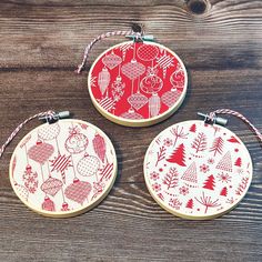 three red and white christmas ornaments hanging from string on wooden table with wood planks