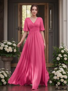 a woman in a long pink dress standing on a porch with white flowers behind her