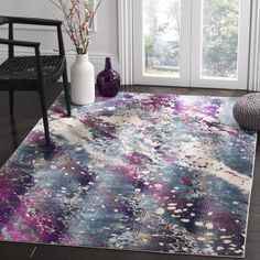 a colorful area rug in front of a window with a chair and vase on the floor