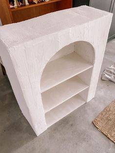 a white shelf sitting on top of a cement floor next to a rug and wooden shelves