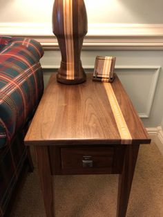 a wooden table with a lamp on it next to a plaid couch and end table