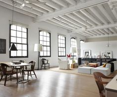 an open living room and dining area with white walls, wood floors and exposed ceilings