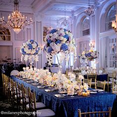 the table is set up with blue and white flowers in vases, candles and chandeliers