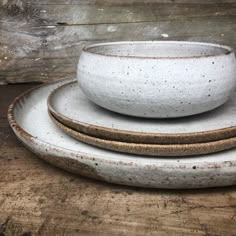 three white dishes stacked on top of each other in front of a wooden tablecloth