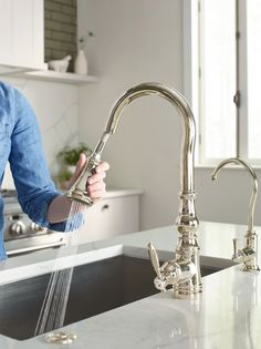 a woman washing her hands under a kitchen faucet with water running from it