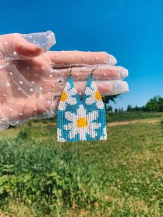 a pair of blue and yellow beaded earrings hanging from a string in a field