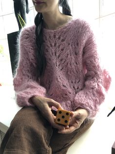 a woman with long hair sitting on a counter holding a dice in her hands while wearing a pink sweater