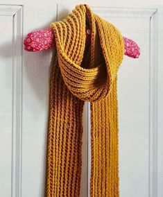 a yellow scarf hanging on a white door with pink flowers in the corner and an orange knitted handle