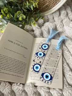 an open book sitting on top of a white blanket next to a plant with blue eyes