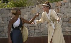 two women standing next to each other in front of a stone wall