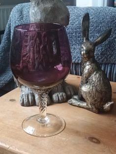 a wine glass sitting on top of a wooden table next to a rabbit figurine