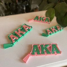 three pink and green aka letters sitting on top of a white table