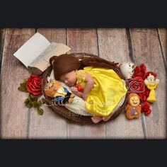 a baby doll laying in a basket next to stuffed animals and books on a wooden floor