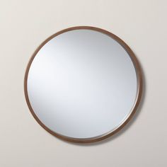 a round mirror hanging on the wall next to a white wall with a wooden frame