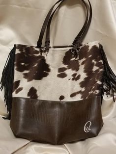 The Brown Cow bag is 13" wide, 15 1/2" tall and 4" deep (front to back) with brown tassels on the side. It is a faux cow hide and faux leather. Lined with linen and 2 interior pockets. Brown Faux Leather Satchel With Double Handle, On-the-go Faux Leather Tote Bag, Faux Leather Tote Bag For Errands, Faux Leather Tote Bag For On-the-go, Brown Faux Leather Bag With Leather Handles, Brown Faux Leather Bucket Bag With Double Handle, Faux Leather Tote Satchel, Brown Faux Leather Tote Bag, Brown Faux Leather Satchel For Errands