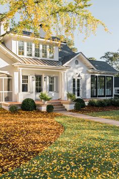 a white house with black shutters and windows on the front porch is surrounded by autumn leaves