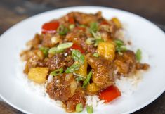 a white plate topped with rice and meat on top of a wooden table next to a fork