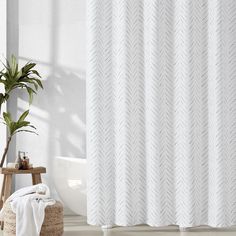 a white shower curtain in a bathroom next to a potted plant and wooden stool