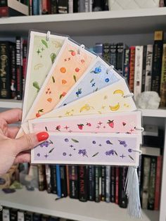 a person holding five different colored papers in front of a book shelf filled with books