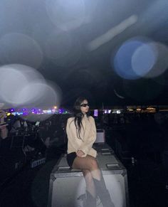 a woman sitting on top of a metal box in front of a crowd at night